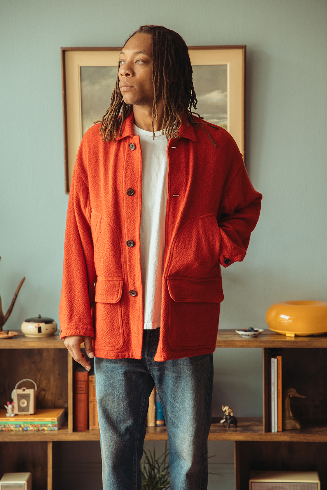 Man wearing a red coat standing in front of a blue wall.