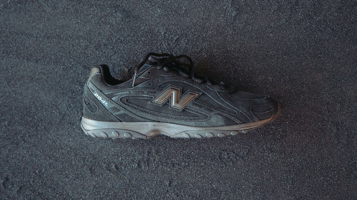 black New Balance sneaker laying in black sand