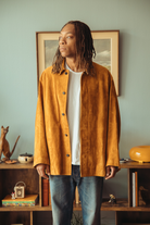 man wearing suede jacket standing in front of a blue wall.