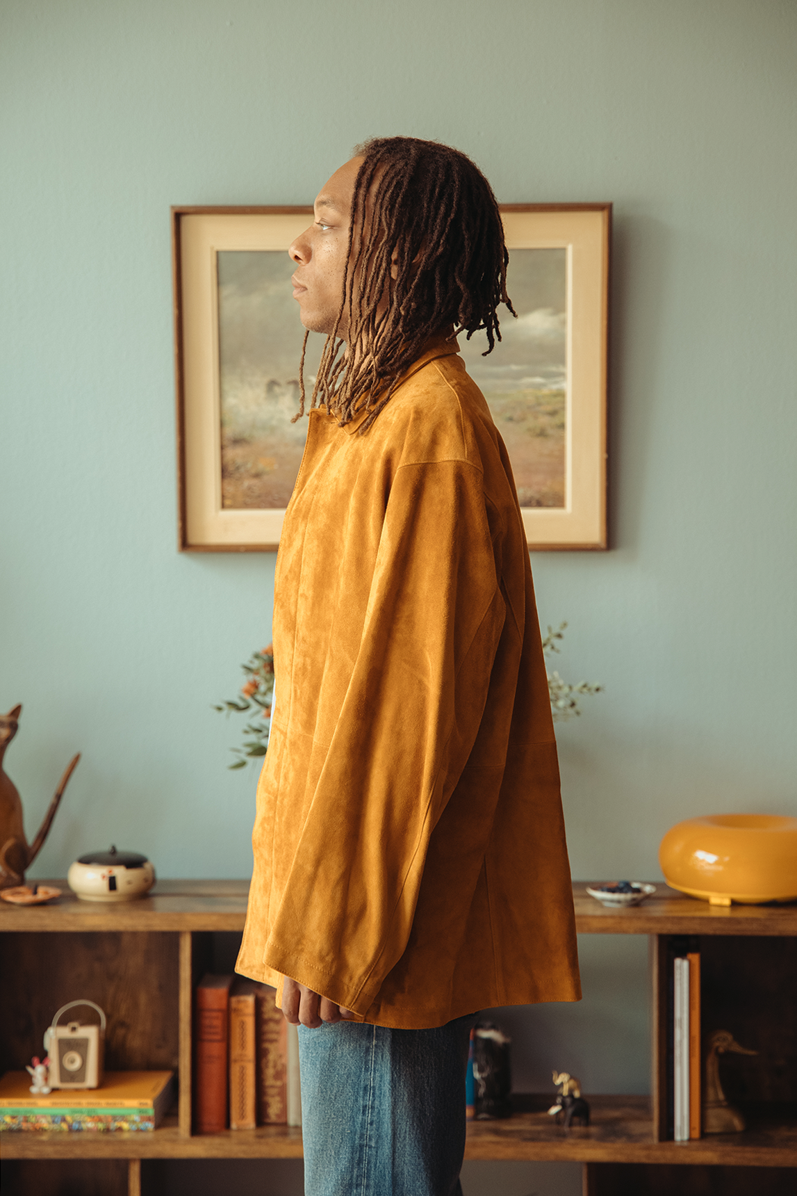 Profile of a man wearing suede jacket standing in front of a blue wall.