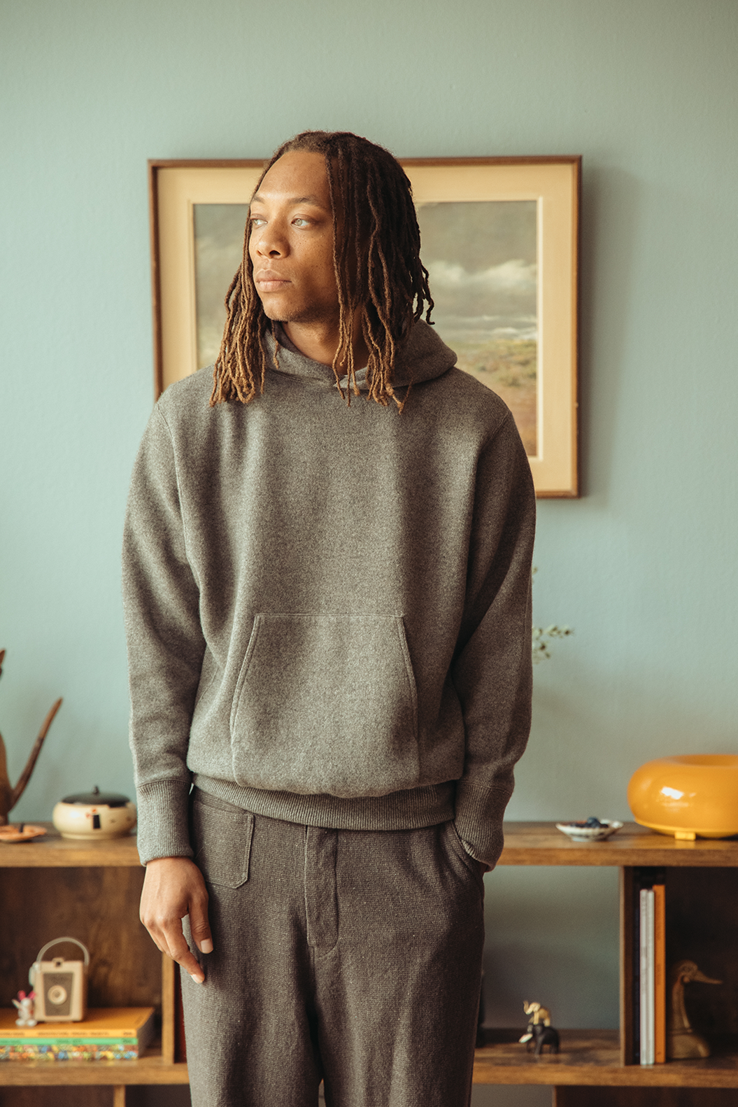 Man wearing a grey hoodie standing in front of a blue wall.