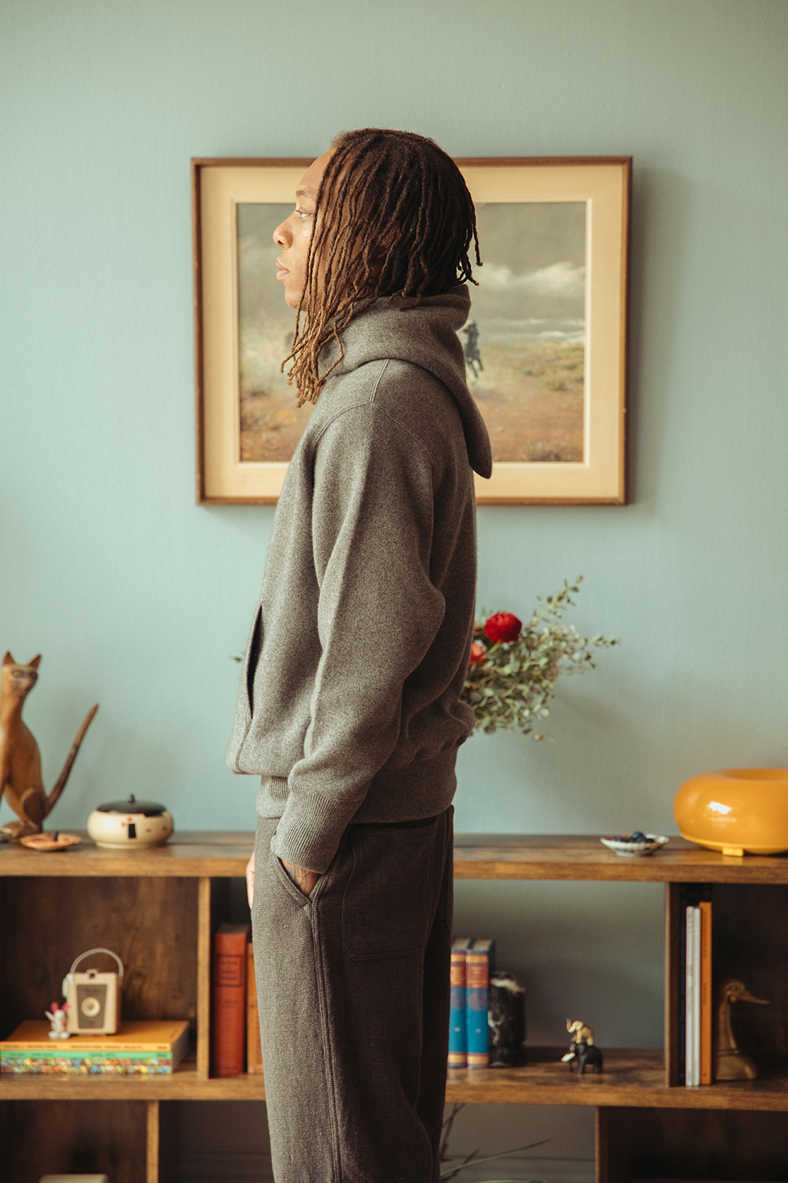 Profile of a man wearing a grey hoodie standing in front of a blue wall.