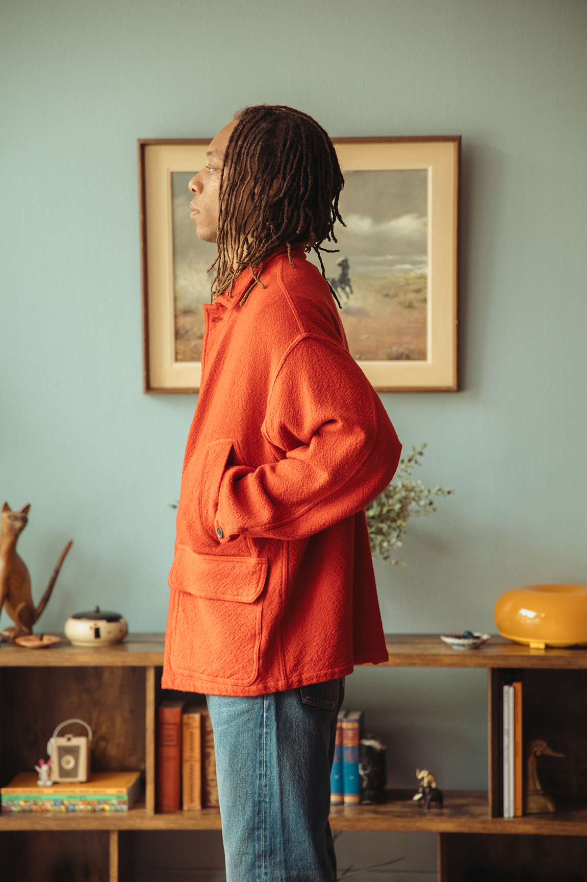 Profile shot of a man wearing a red coat standing in front of a blue wall.